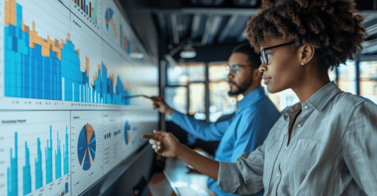 Two individuals analyze various colorful charts and graphs on a large screen in a modern office setting, leveraging artificial intelligence to refine their business strategy.